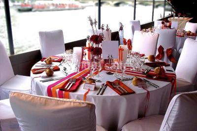 Terrasse d'un bateau avec des fauteuils, des plantes décoratives et une vue sur un pont et des arbres en arrière-plan.