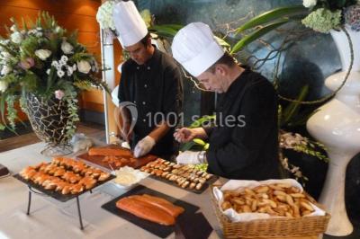 Terrasse d'un bateau avec des fauteuils, des plantes décoratives et une vue sur un pont et des arbres en arrière-plan.