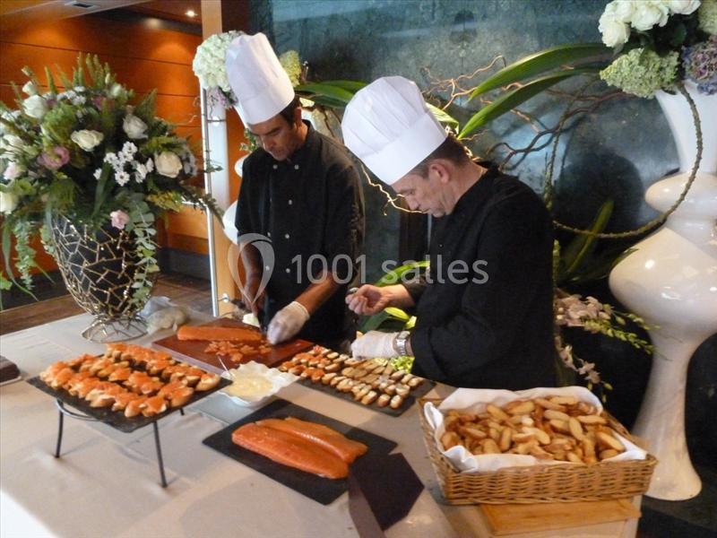 Deux chefs préparent des plats de saumon et des amuse-bouches sur une table garnie de fleurs et de décorations.