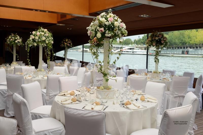 Salle de réception élégante avec tables rondes décorées de nappes blanches et centres de table fleuris près d'une baie…