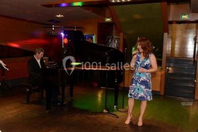 Terrasse d'un bateau avec des fauteuils, des plantes décoratives et une vue sur un pont et des arbres en arrière-plan.