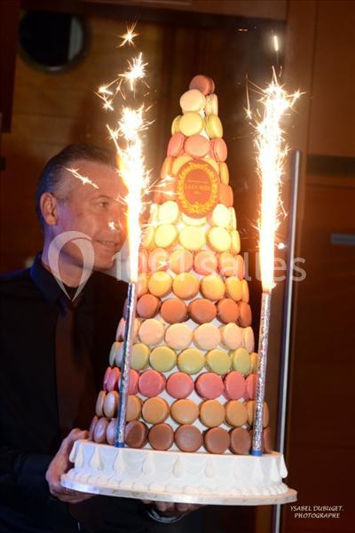 Tour de macarons colorés en forme de pyramide, décorée de cierges magiques allumés, tenue par un homme.