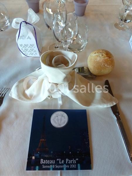 Serviette pliée en forme de rose, menu et pain disposés sur une table dressée avec couverts et verres.