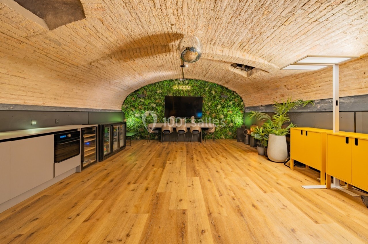 Salle voûtée avec parquet, mur végétal, table de réunion, meubles modernes et éclairage chaleureux.