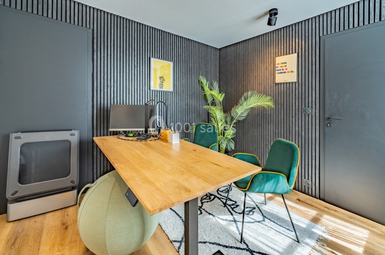Bureau moderne avec table en bois, chaise, écran d'ordinateur, plantes vertes et murs noirs texturés.