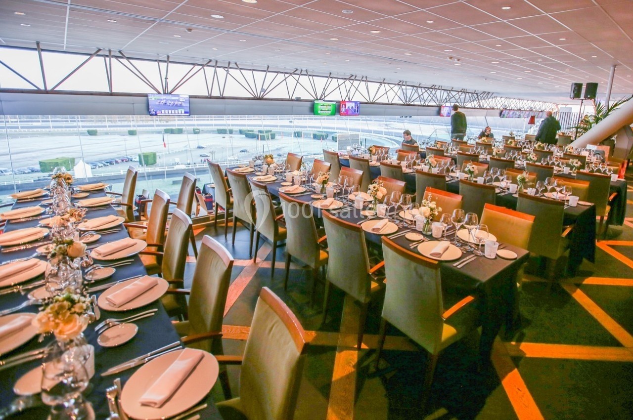Salle de réception avec de longues tables dressées, vue sur un espace extérieur à travers de grandes baies vitrées.