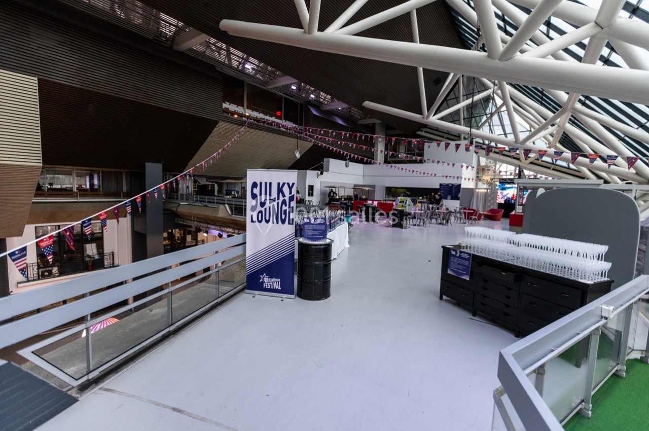 Espace intérieur lumineux avec des tables, des chaises, des guirlandes et un panneau indiquant ’Sulky Lounge’.