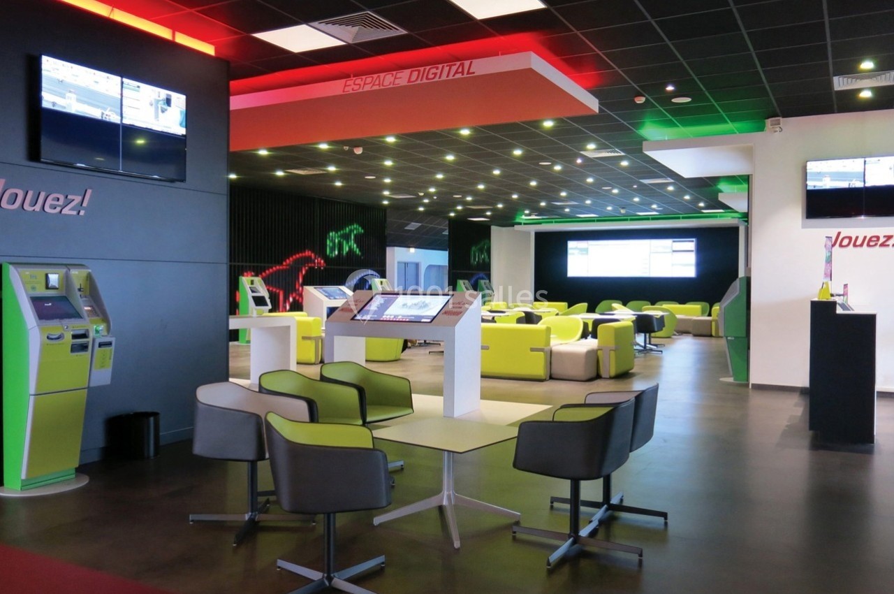 Salle moderne avec bornes interactives, écrans numériques et sièges colorés dans un espace lumineux et technologique.