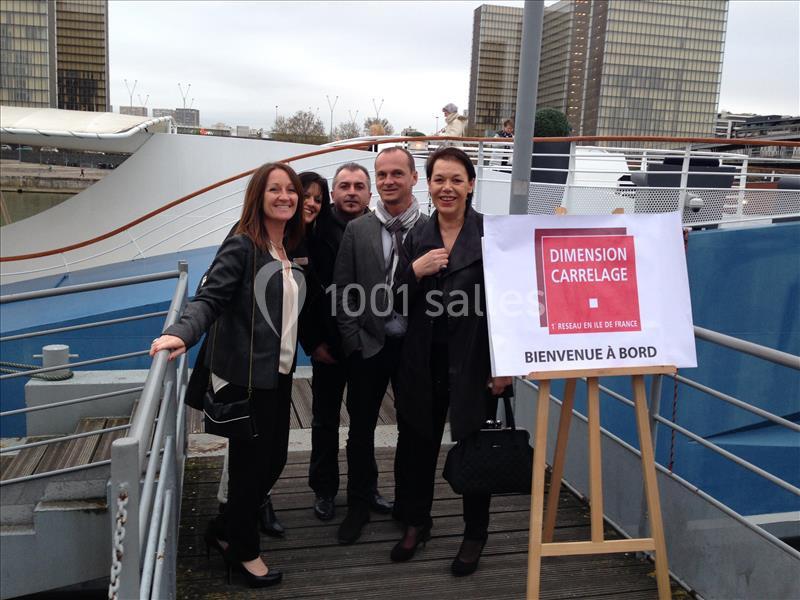 Un groupe de personnes souriantes posant sur un ponton près d'un panneau ’Bienvenue à bord’ et ’Dimension Carrelage’.