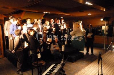 Un groupe de personnes pose sur une scène éclairée, accompagné d'une mascotte en costume d'ours.