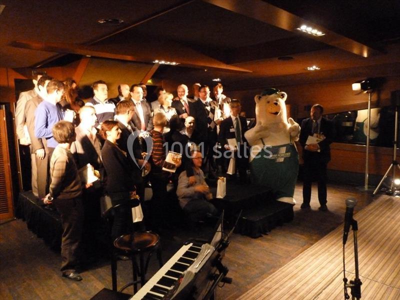 Un groupe de personnes pose sur une scène éclairée, accompagné d'une mascotte en costume d'ours.