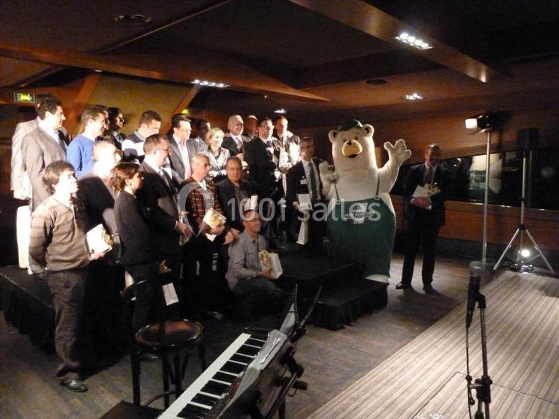 Un groupe de personnes posant sur une scène avec une mascotte en costume d'ours dans une salle éclairée.