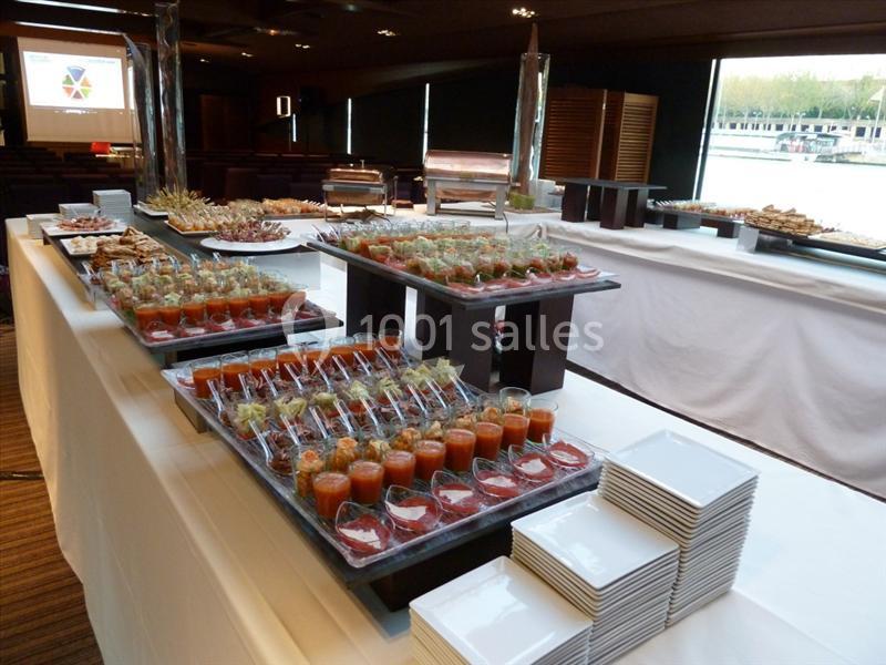Buffet avec verrines et plats variés disposés sur des tables couvertes de nappes blanches dans une salle lumineuse.