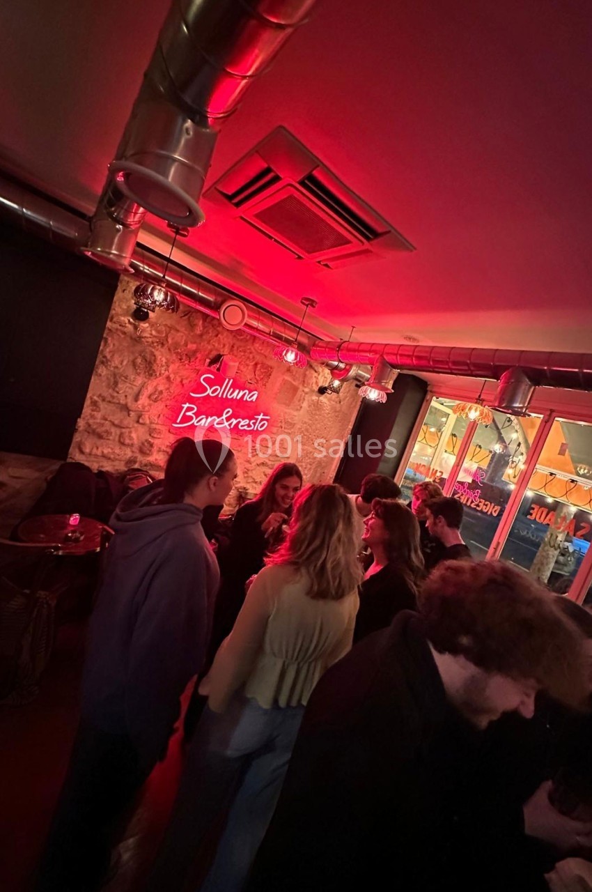 Groupe de personnes discutant dans un bar à l'ambiance tamisée avec un néon rouge au mur.