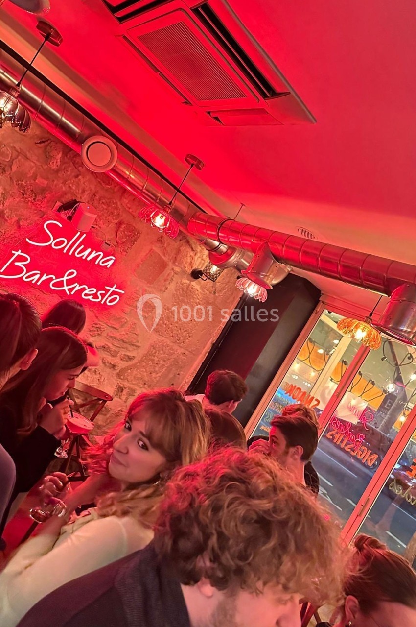 Groupe de personnes dans un bar à l'éclairage rouge, avec un mur en pierre et une enseigne lumineuse ’Solluna Bar & Resto’.