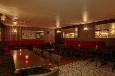 Salle de restaurant chaleureuse avec banquettes rouges, tables en bois sombre et éclairage tamisé par des bougies.