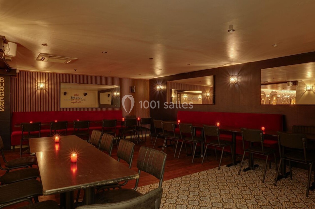 Salle de restaurant chaleureuse avec éclairage tamisé, tables en bois, chaises noires et banquettes rouges.