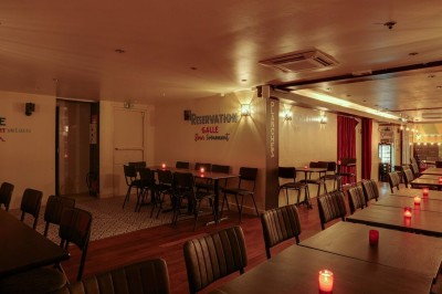 Salle de restaurant chaleureuse avec banquettes rouges, tables en bois sombre et éclairage tamisé par des bougies.