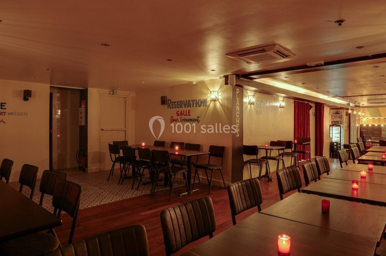 Salle de restaurant chaleureuse avec tables alignées, éclairage tamisé et bougies rouges sur chaque table.