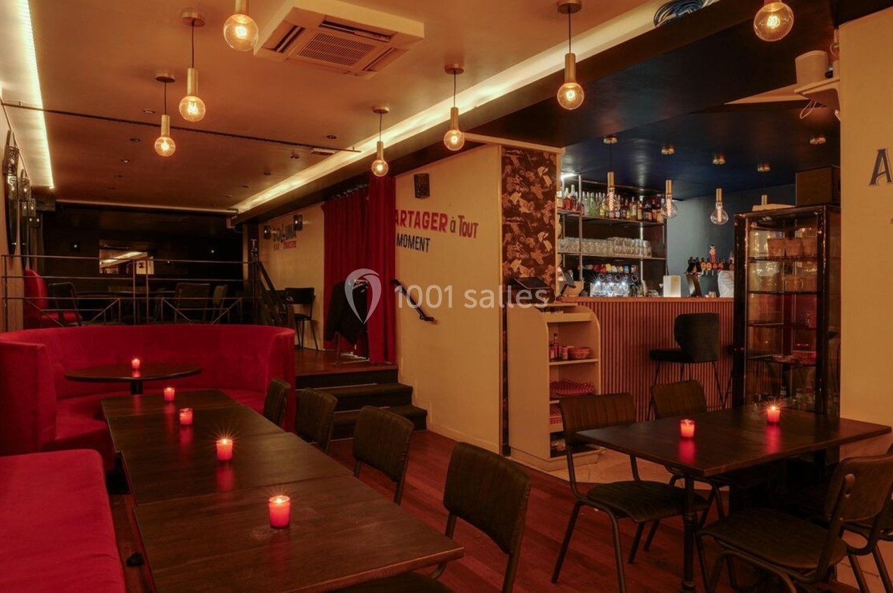 Salle de restaurant chaleureuse avec éclairage tamisé, tables en bois, banquettes rouges et bougies allumées.