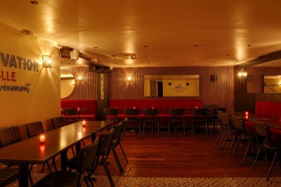 Salle de restaurant chaleureuse avec banquettes rouges, tables en bois sombre et éclairage tamisé par des bougies.