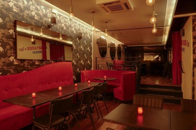 Salle de restaurant chaleureuse avec banquettes rouges, tables en bois sombre et éclairage tamisé par des bougies.