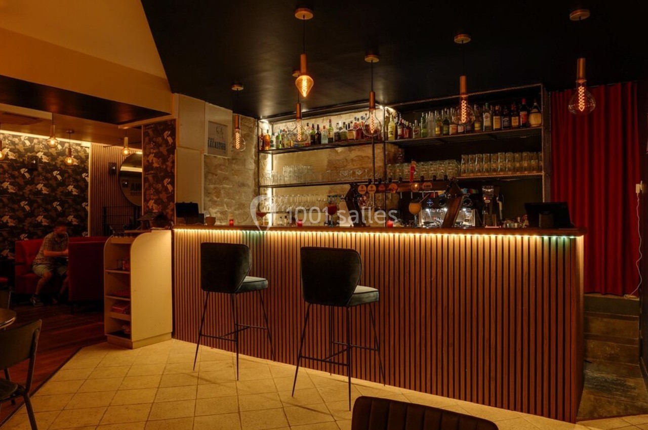 Bar chaleureux avec comptoir éclairé, tabourets hauts, étagères garnies de bouteilles et ambiance tamisée.