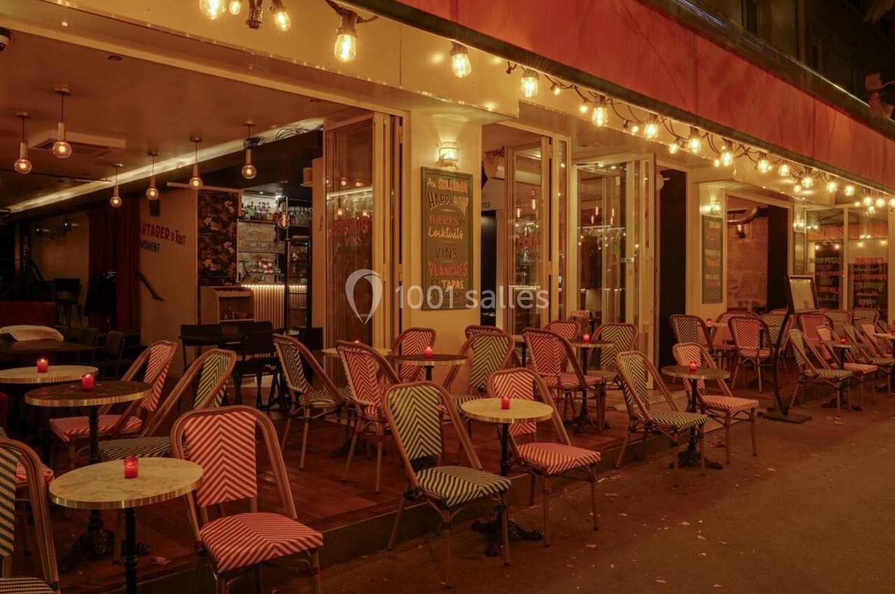 Terrasse d'un café-restaurant éclairée par des guirlandes lumineuses, avec des chaises et tables alignées en soirée.