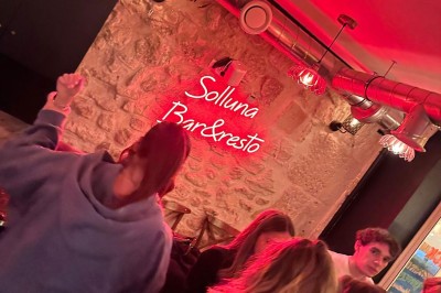 Terrasse d'un restaurant avec chaises en osier et tables dressées, éclairée par des guirlandes lumineuses en soirée.