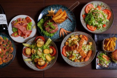 Terrasse d'un restaurant avec chaises en osier et tables dressées, éclairée par des guirlandes lumineuses en soirée.