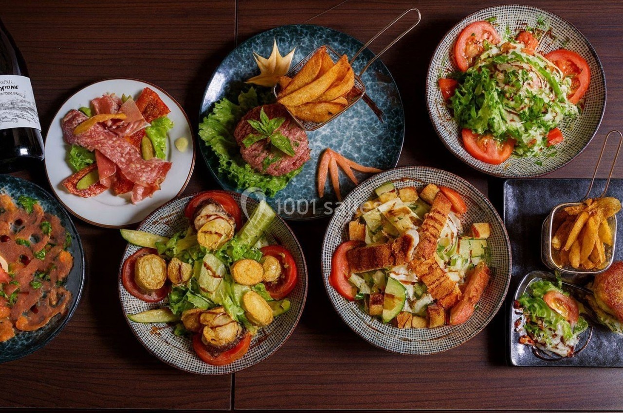 Assortiment de plats comprenant salades, charcuterie, frites et tartare, disposés sur une table en bois.