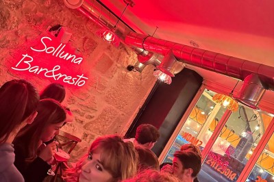 Terrasse d'un restaurant avec chaises en osier et tables dressées, éclairée par des guirlandes lumineuses en soirée.