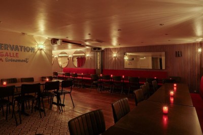 Terrasse d'un restaurant avec chaises en osier et tables dressées, éclairée par des guirlandes lumineuses en soirée.