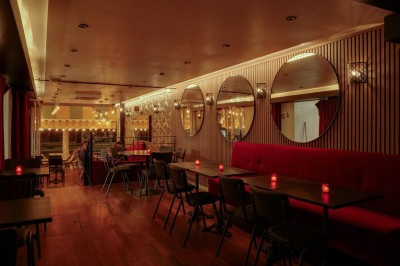 Terrasse d'un restaurant avec chaises en osier et tables dressées, éclairée par des guirlandes lumineuses en soirée.