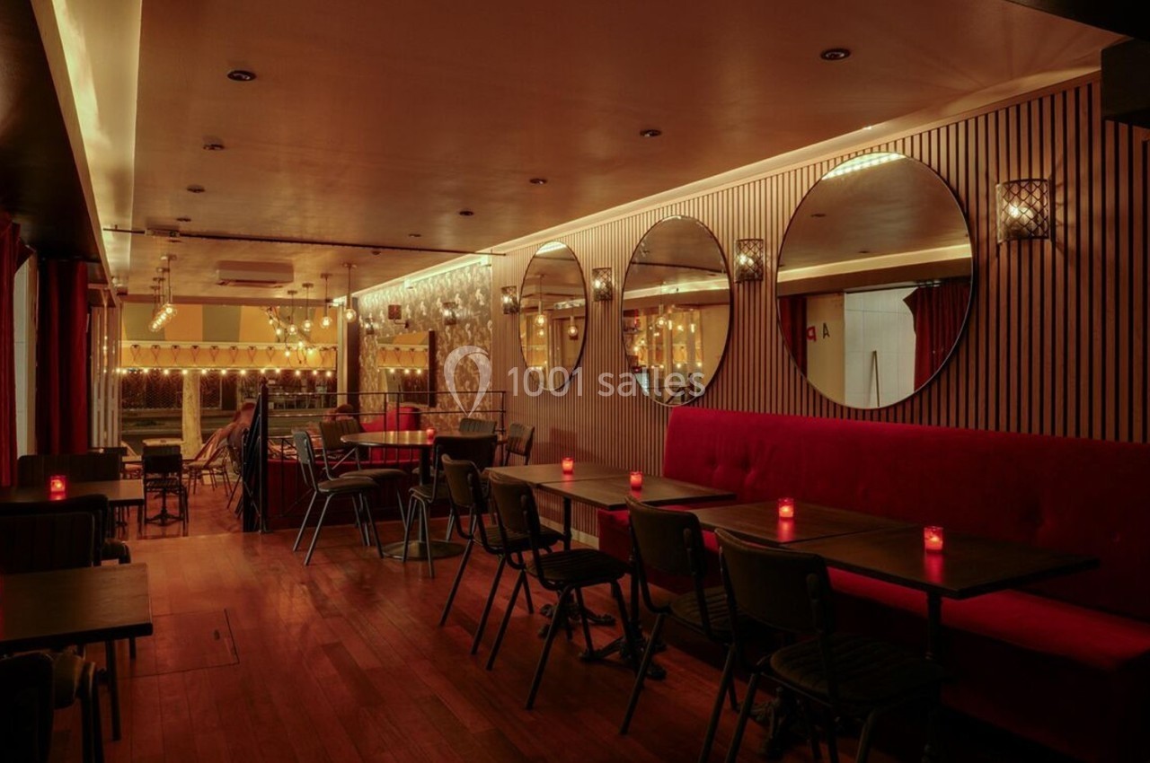 Salle de restaurant chaleureuse avec tables en bois, banquettes rouges, miroirs ronds et éclairage tamisé.