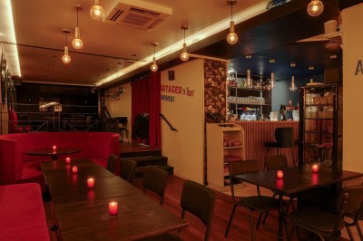 Terrasse d'un restaurant avec chaises en osier et tables dressées, éclairée par des guirlandes lumineuses en soirée.