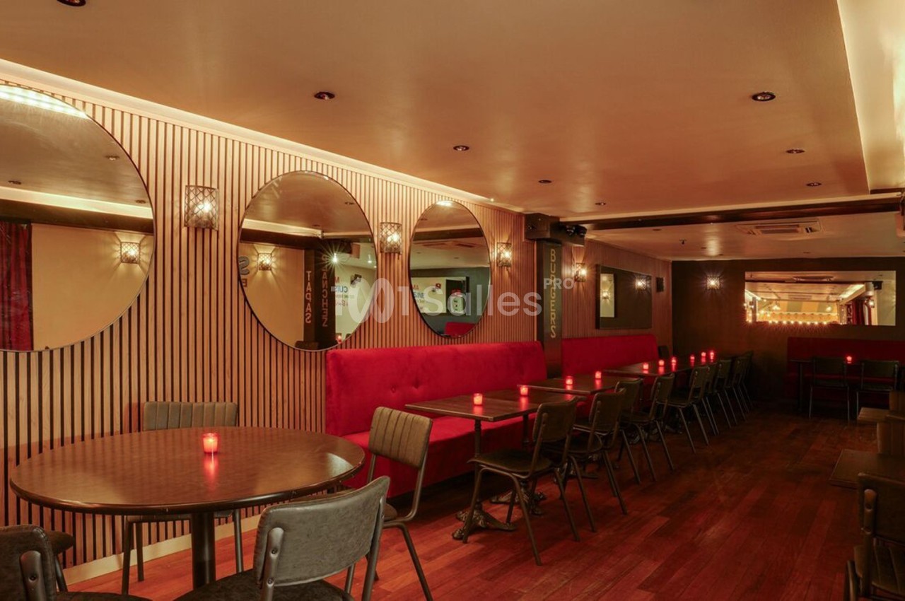 Salle de restaurant avec tables rondes, chaises noires, banquettes rouges, miroirs circulaires et éclairage tamisé.