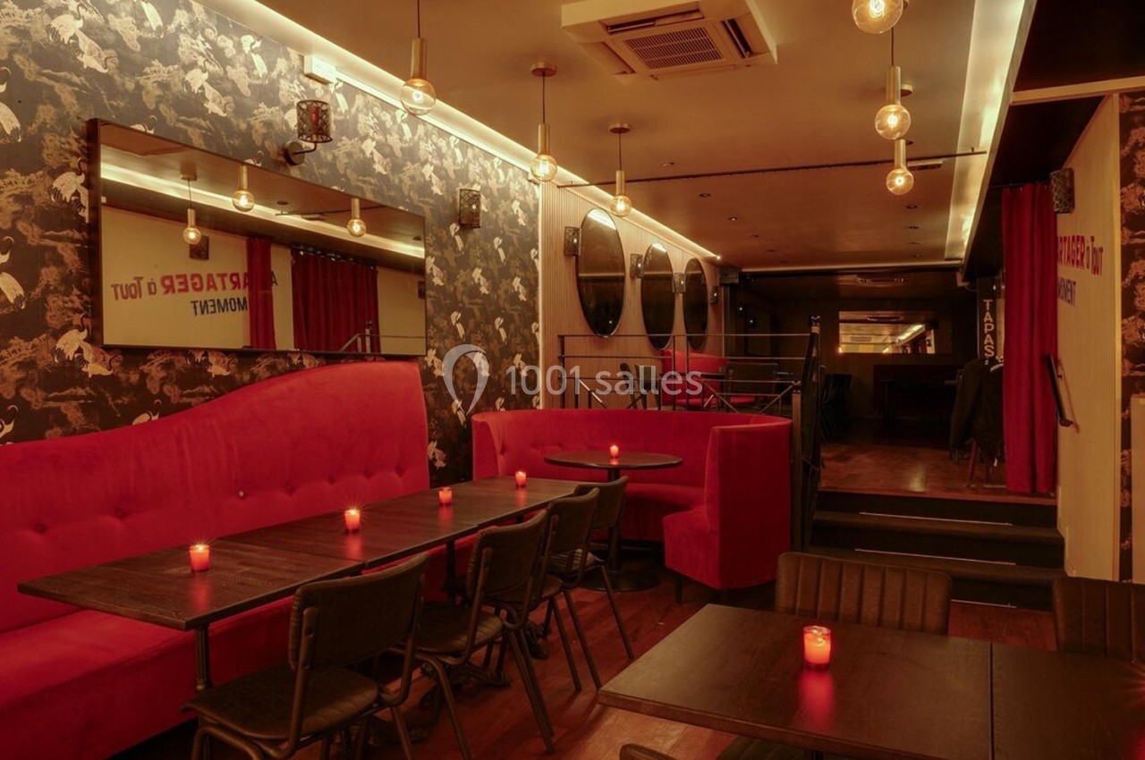 Salle de restaurant avec banquettes rouges, tables en bois sombre, éclairage tamisé et décorations murales sombres.