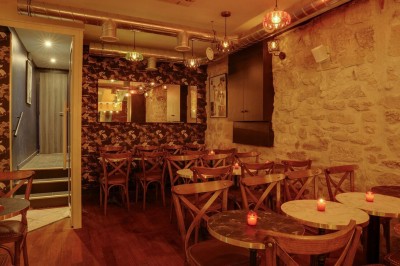Terrasse d'un restaurant avec chaises en osier et tables dressées, éclairée par des guirlandes lumineuses en soirée.