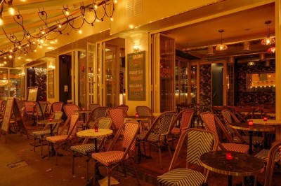Terrasse d'un restaurant avec chaises en osier et tables dressées, éclairée par des guirlandes lumineuses en soirée.