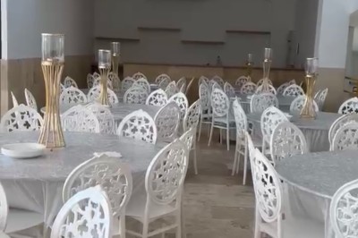 Salle de réception lumineuse avec tables dressées, chaises blanches décorées et tapis rouges dans un espace spacieux.