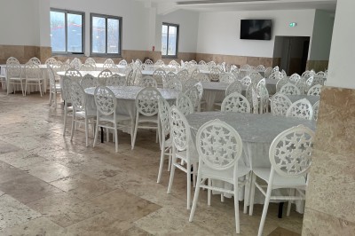 Salle de réception lumineuse avec tables dressées, chaises blanches décorées et tapis rouges dans un espace spacieux.