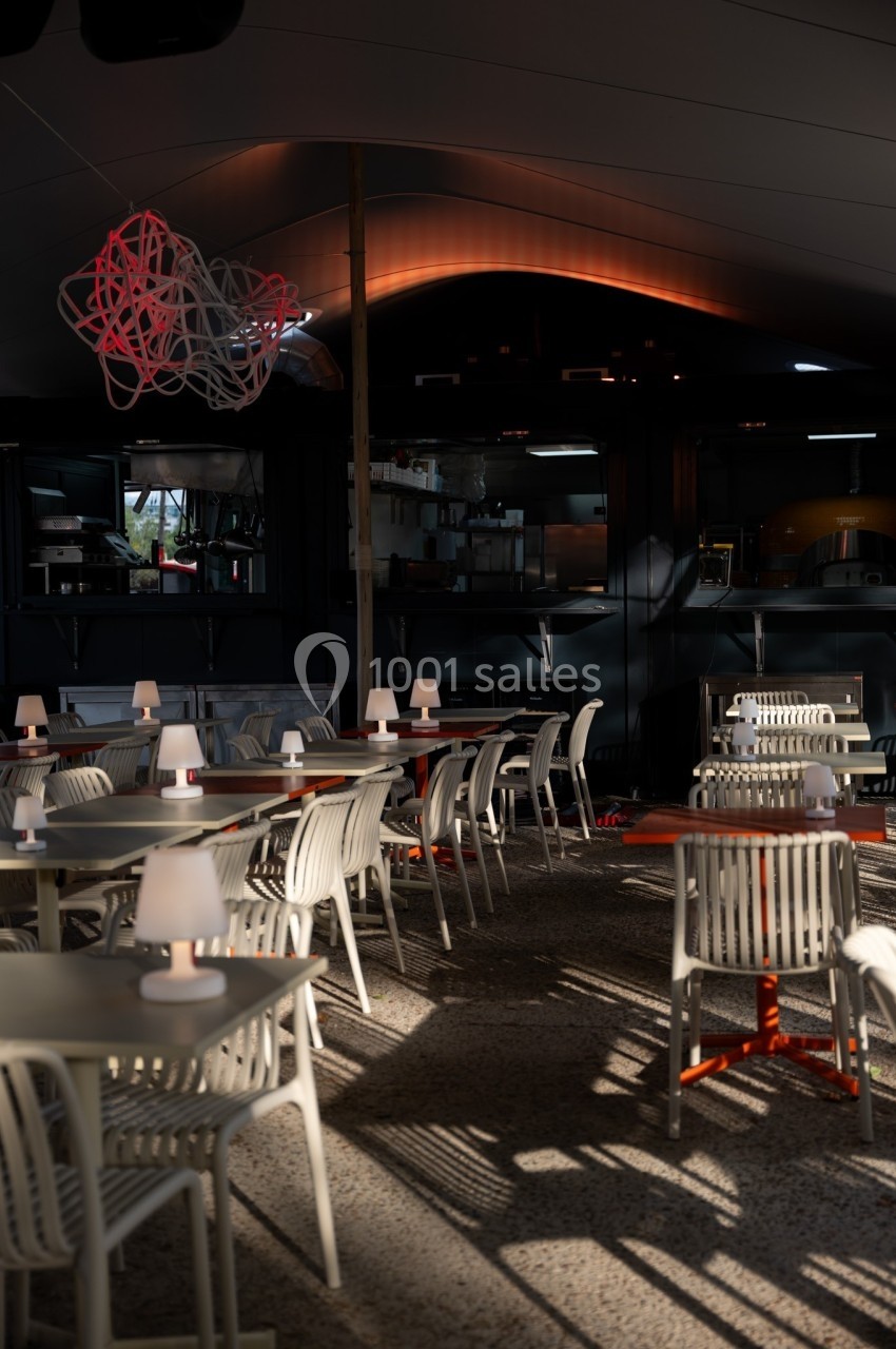 Salle de restaurant moderne avec tables et chaises blanches, éclairée par une lumière tamisée en fin de journée.