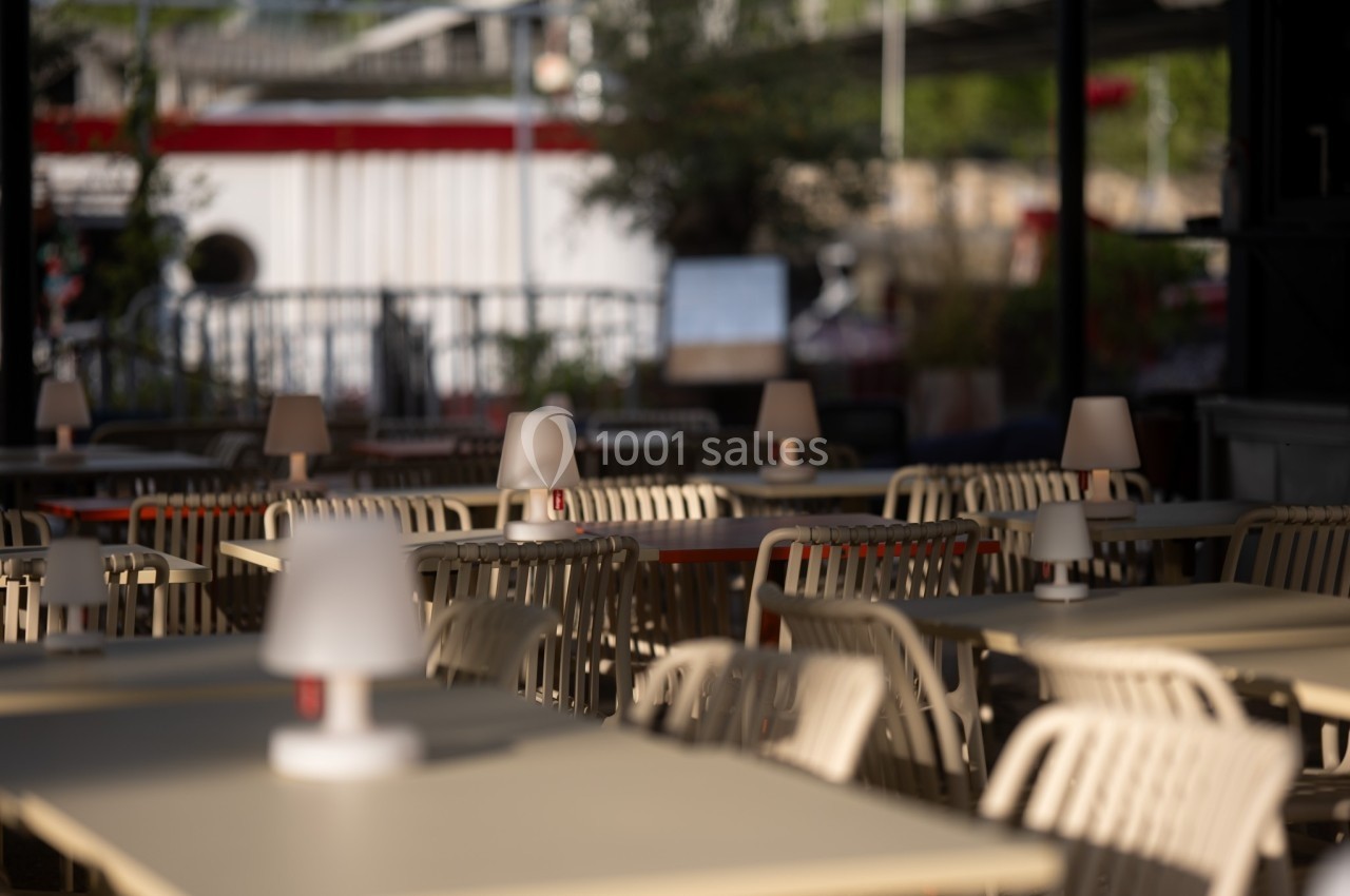 Terrasse de restaurant avec des tables et chaises vides, éclairées par des lampes de table en plein air.