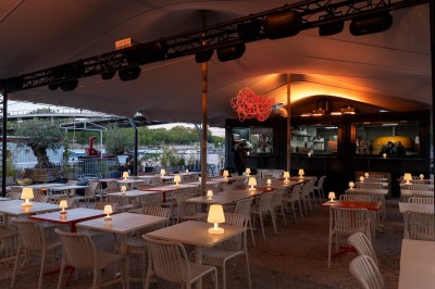 Vue d'un quai animé avec des stands colorés sous des tentes, près d'un bâtiment moderne et d'un cours d'eau.