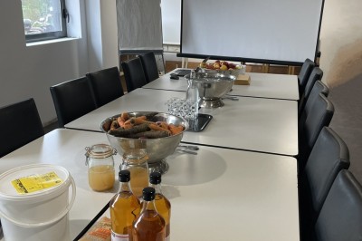 Salle de réunion avec une table dressée contenant des boissons, fruits, viennoiseries et matériel de présentation.