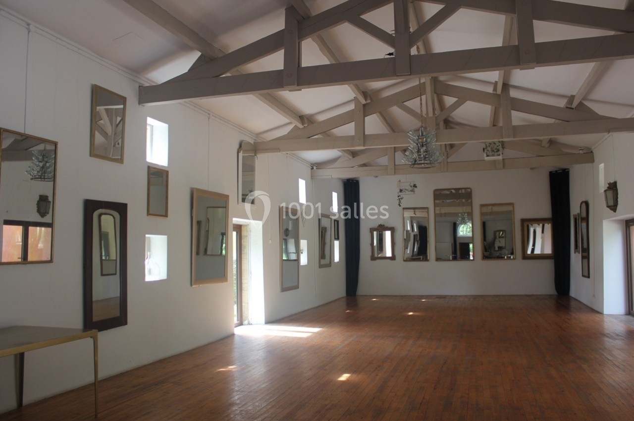 Salle lumineuse avec parquet en bois, murs blancs ornés de nombreux miroirs et poutres apparentes au plafond.