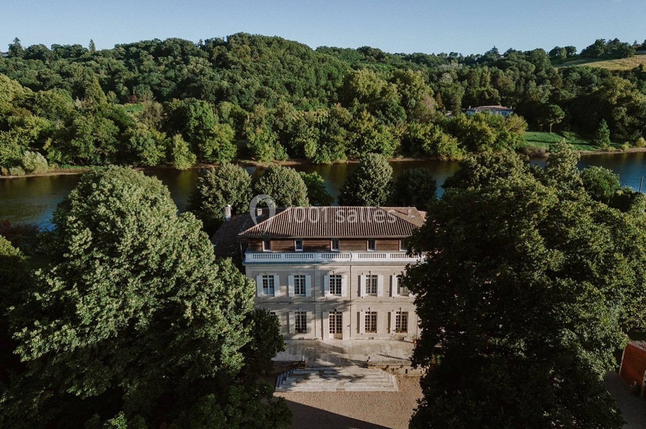 Manoir entouré d'arbres, situé près d'une rivière, sous un ciel dégagé.