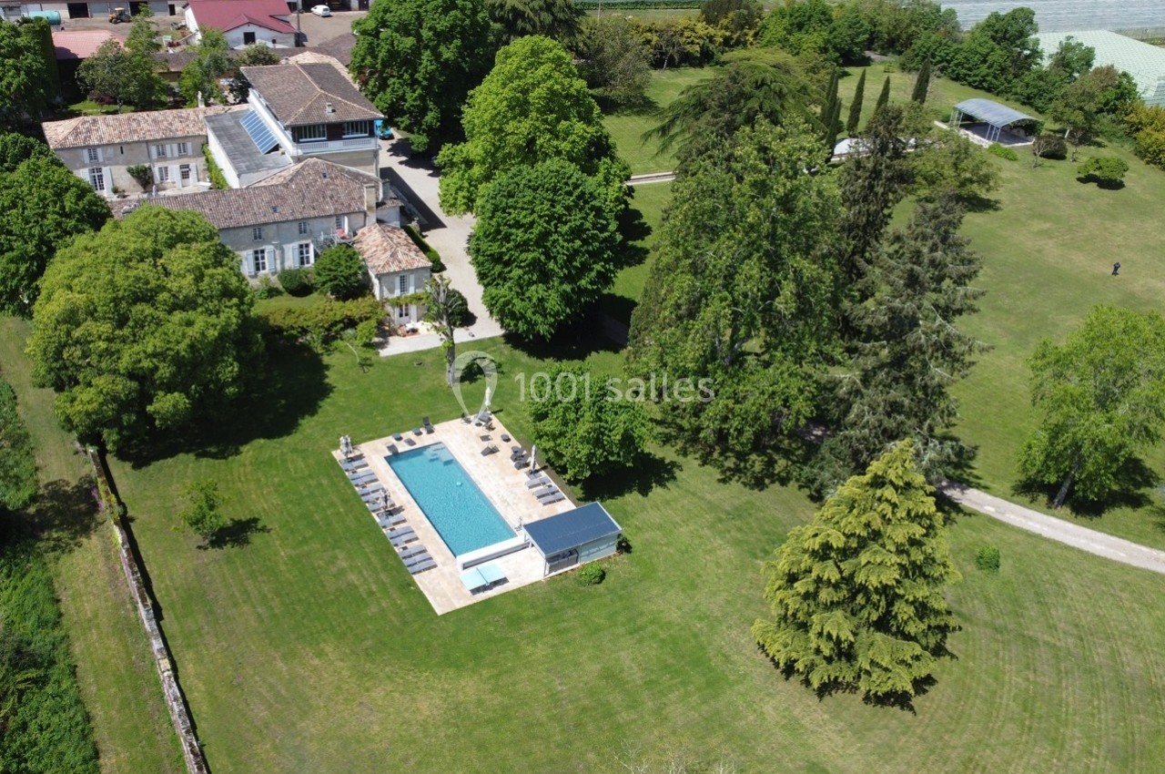 Vue aérienne d'une propriété avec piscine, entourée de vastes espaces verts, d'arbres et de bâtiments.