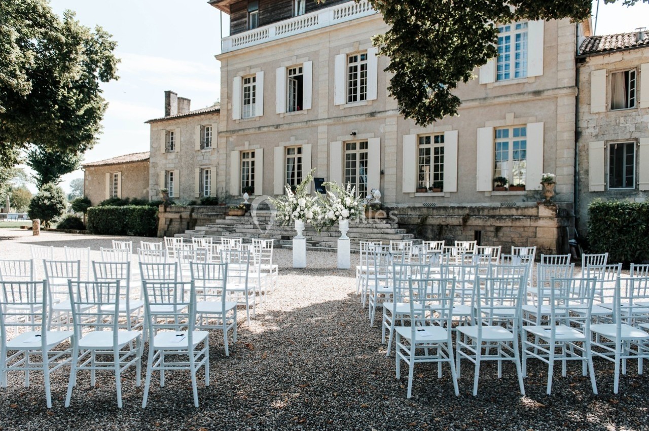 Chaises blanches disposées en extérieur devant un bâtiment en pierre, préparées pour une cérémonie.